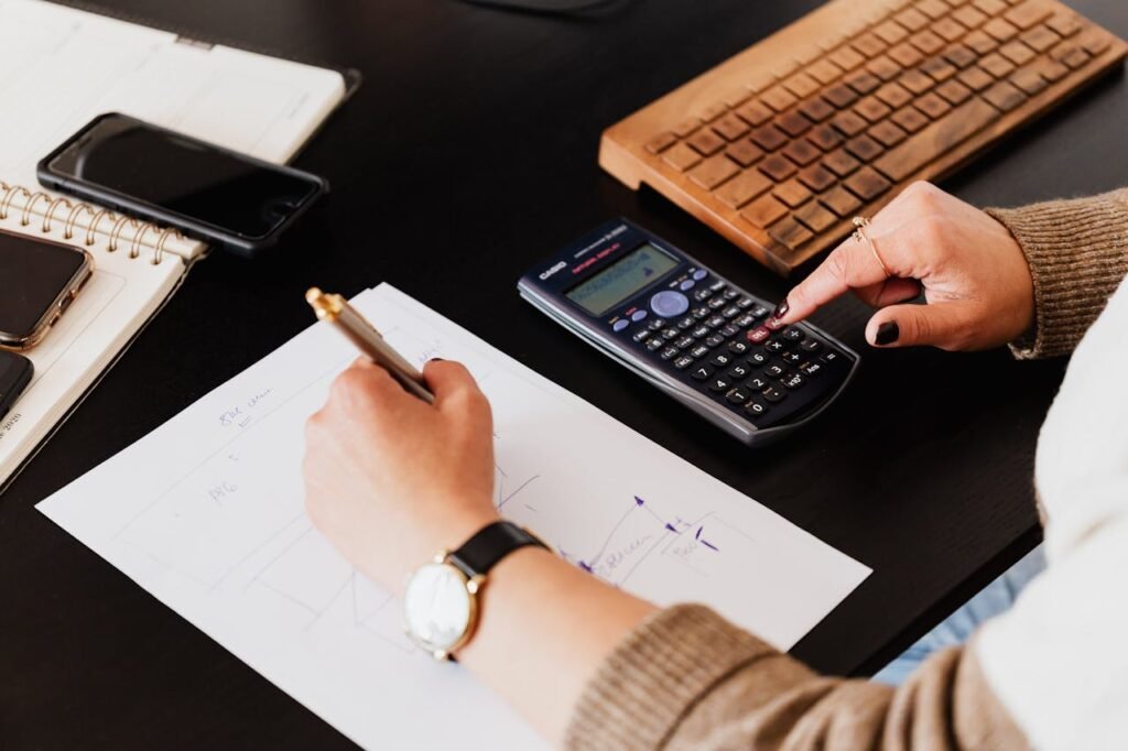 Close-up of hands working with a calculator and notebook on a desk, analyzing documents.